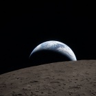 Key Art for the 2025- 2026 Podcast Episodes features the Earthset captured through the Orion spacecraft window at 6:41 p.m. EDT, April 6, 2026, during the Artemis II crew&rsquo;s flyby of the Moon. A muted blue Earth with bright white clouds sets behind the cratered lunar surface. The dark portion of Earth is experiencing nighttime. On Earth&rsquo;s day side, swirling clouds are visible over the Australia and Oceania region. In the foreground, Ohm crater has terraced edges and a flat floor interrupted by central peaks&mdash;formed when the surface rebounded upward during the impact that created the crater. Image Credit: NASA. 