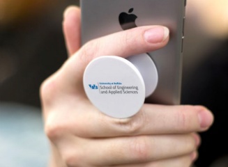 A cellphone pop-socket with the School of Engineering brand extension mark. 
