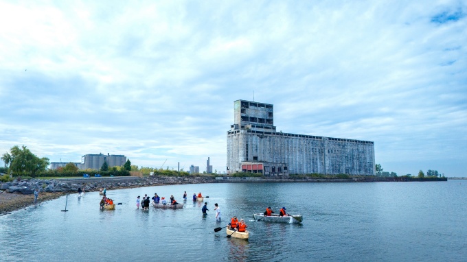 Architecture students in handmade canoes paddle near a grain elevator at Gallagher beach. 