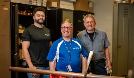 Maintenance men pose in front of piping. 