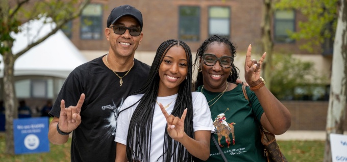 Two parents with students on move-in day holding up their horns up hands.