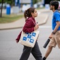 Female student crossing the street holding her Campus Living Icons bag. 