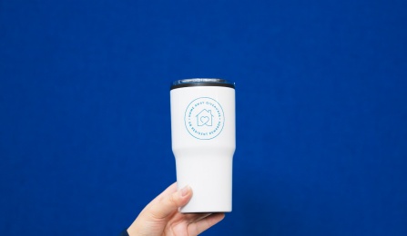 Hand holding white thermos with home away giveaway logo on it. House icon with circlng text.