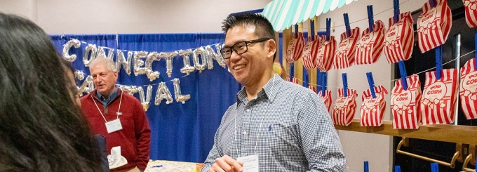 UB alum talking to a student while standing in front of a wall of red and white popcorn bags. 
