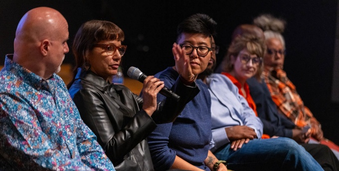 Woman holding a microphone while sitting in the audience. 