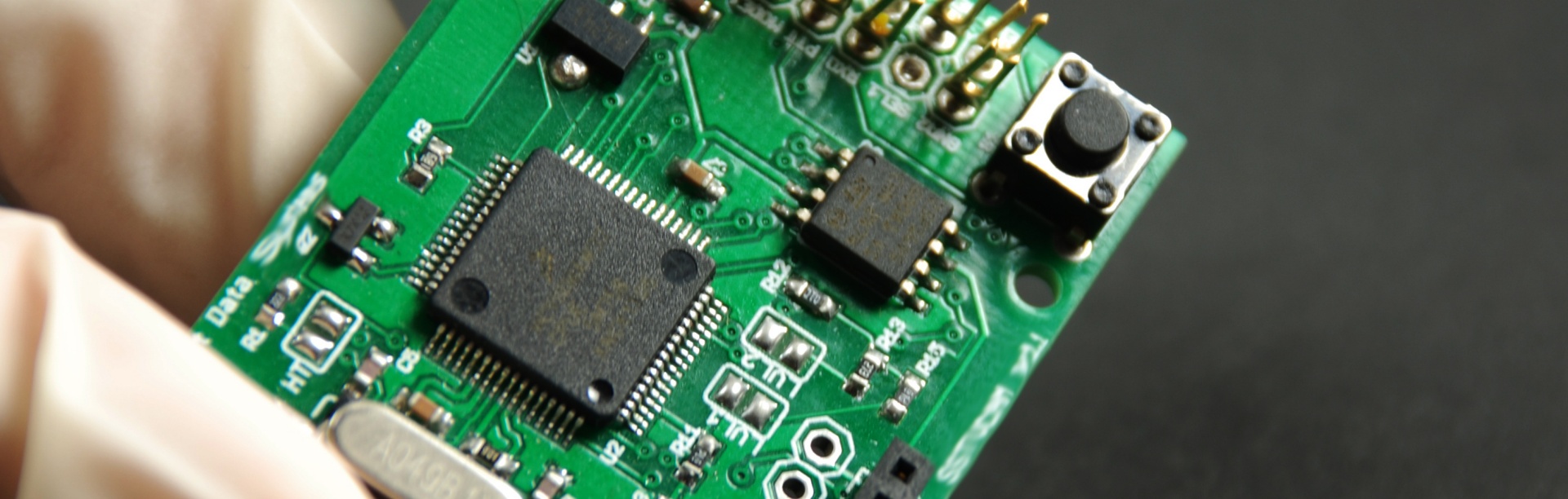 Zoomed in shot of tools (forceps and pointed pen-like object) on top of a computer chip. 