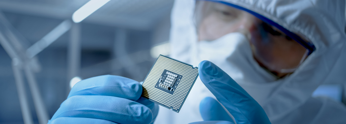 A person examines a microchip in full lab gear. 