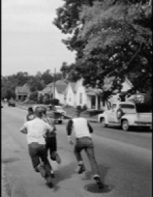 Three white male students chase an African American male student, a member of the “Little Rock Nine,” down a neighborhood street in Arkansas in the 1940’s.