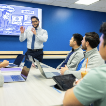 An instructor presenting to a group of students around a table.