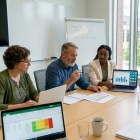 University faculty reviewing assessment data on laptops and documents, connecting assignments, portfolios and other evidence into an organized, unified system in a collaborative academic setting. 