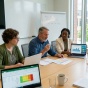 University faculty reviewing assessment data on laptops and documents, connecting assignments, portfolios and other evidence into an organized, unified system in a collaborative academic setting. 