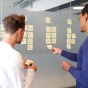 Image of two people putting post-it notes on a wall. 