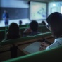 A dark classroom with a professor using digital materials presented on projector screens. 
