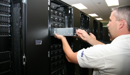 Male technician slides server out of a rack in a data center with many racks of servers. 