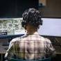 Student with headgear connected to a computer screen, looking at two screens. 