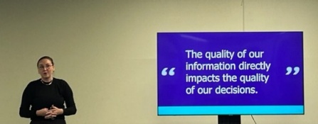 Image of a presenter next to a screen reading "The quality of our informataion directly impact the quality of our decisions". 