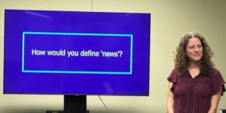 Image of presenter in front of a screen reading "How would you define 'news'". 