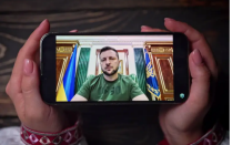 Photo of hands holding a phone showing a video of President Zelenskyy. 