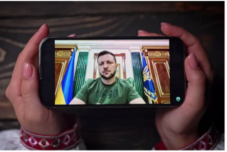 Photo of hands holding a phone showing a video of President Zelenskyy. 