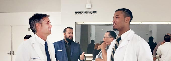 Two men in lab coats and ties, talking and smiling. 