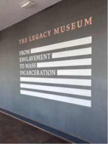 An image on a wall in the shape of a flag and says The Legacy Museum. From enslavement to mass incarceration. 