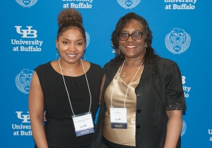 CSTEP Director with Administrative Assistant in front of UB logo backdrop. 