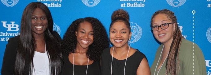 CSTEP Director standing with CSTEP students in front of a UB logo backdrop at the 2018 CSTEP Summer Research Symposium. 