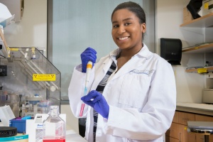 CSTEP student wearing white lab coat and holding test tub in research lab environment. 