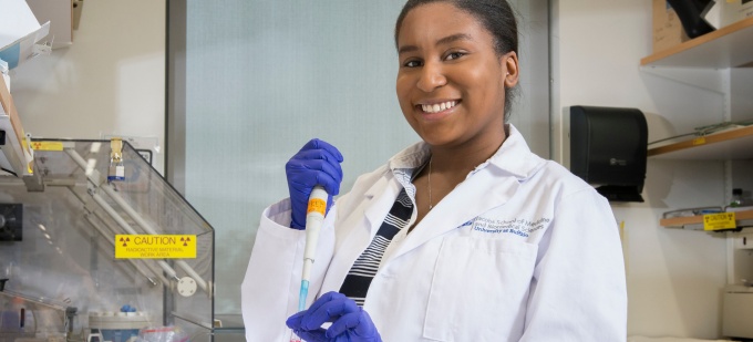 CSTEP student wearing white lab coat and holding test tub in research lab environment. 