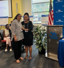 Director standing with faculty research mentor and holding a certificate in front of a UB logo background. 
