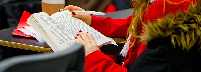 A female student wearing a red shirt, reading a book at a table. 