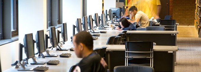 Four students sitting at a row of computers, at a computer lab. 