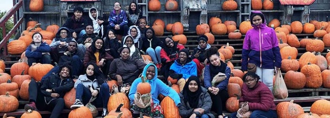 Group of students sitting outside on bleachers with pumpkins surrounding them. 