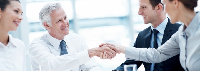 Two people shaking hands at a table with two others. 