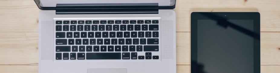 Photo from above of a laptop and tablet on a wooden desk. 