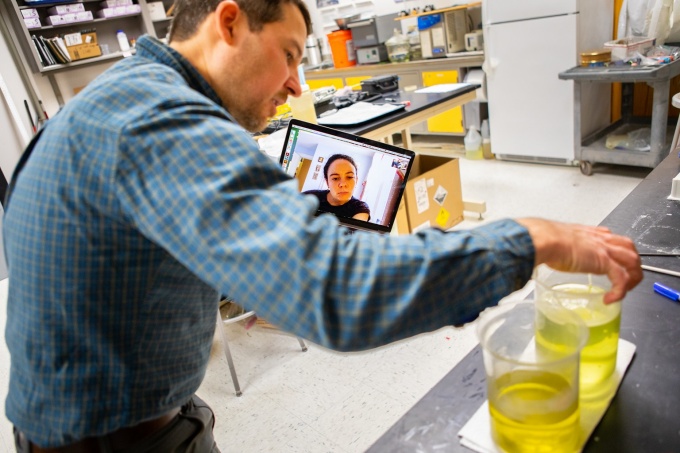 Professor in research lab with remote student engagement. 