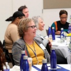 Person smiling sitting at a table listening to others. 