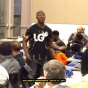 Person standing and speaking while others are seated at Men's Conference. 