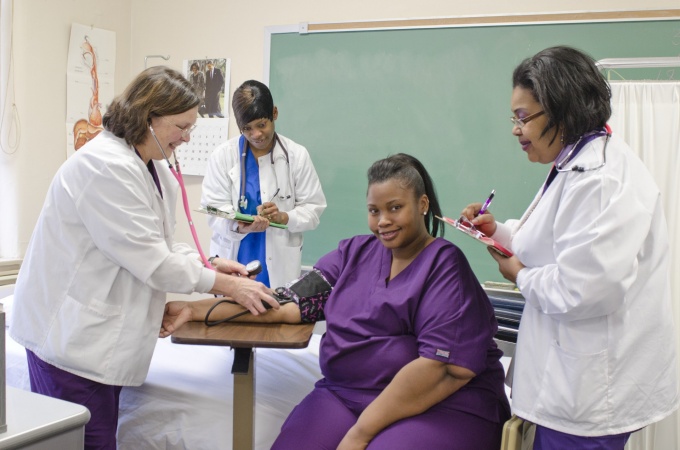 Person sitting having blood pressure taken by three other people. 
