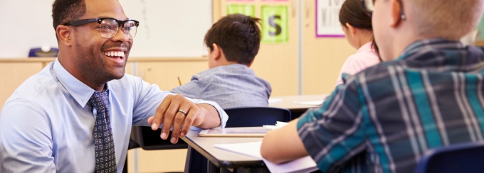 Teacher smiling beside student's desk.