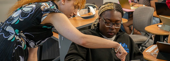 Professor leaning over a student assisting on a tablet.