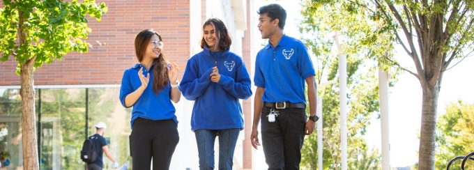 Three student leaders walking and talking in front of a building in the daytime. 