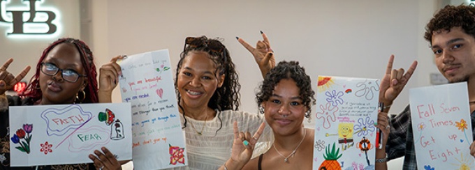 Four students holding up the UB Horns Up sign while showing their community projects.