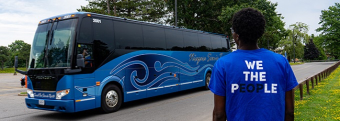 Person looking at a tour arriving and wearing a shirt that says We the People on the back of the shirt. 