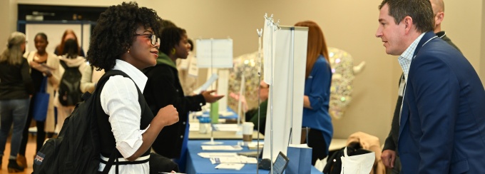 A student is asking a question to a staff member over a table at a tabling event. 