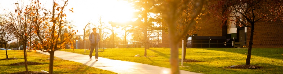 A person walking along a sunlit sidewalk near Hochstetter Hall on UB’s North Campus.