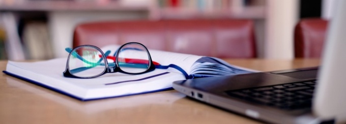 A pair of glasses sitting on top of a notebook in front of a laptop. 