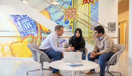 A faculty member speaks with two students. 