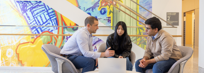 A faculty member speaks with two students. 