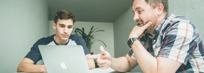 Two people sitting in front of a laptop, speaking. 
